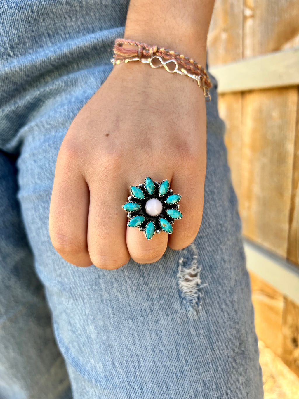 This exquisite ring is the perfect combination of style and craftsmanship. Crafted by Indian artisans, it's made of genuine Sterling Silver with 9 Kingsman Turquoise stones in a beautiful flower design, and features a delicate pink opal center stone. Timelessly elegant and adjustable, this ring lets you express your unique beauty.  Suggested Retail: $250.00