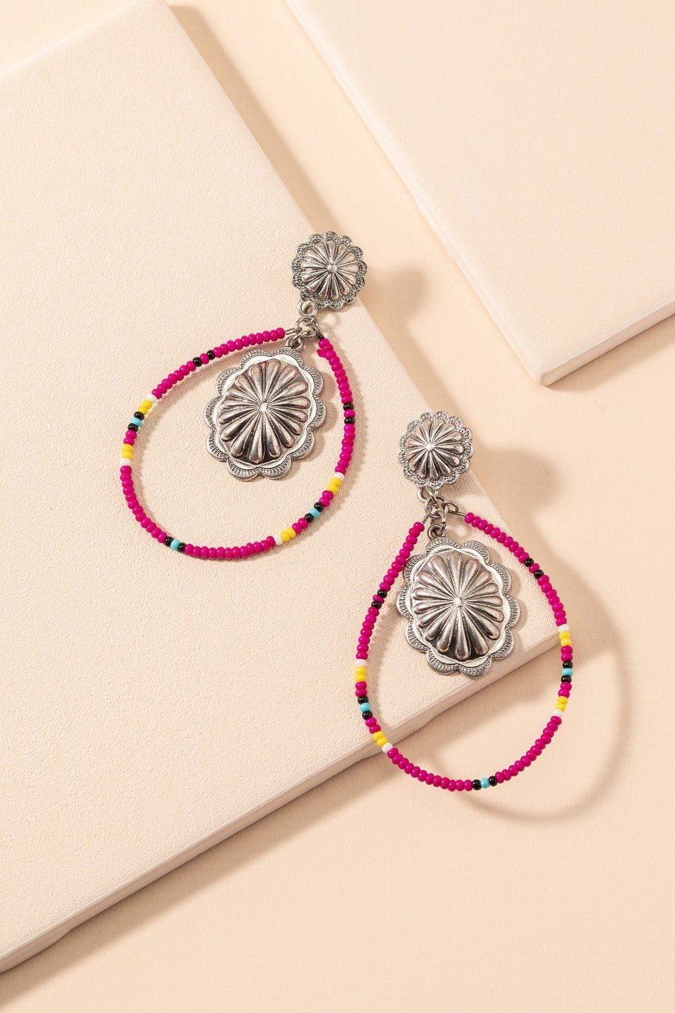Be a wild western flower with these Western Concho Bead Dangle Earrings! Featuring a beaded tear drop shape, with flower silver concho detail - they'll add a touch of cowgirl charm to any look. Crafted from nickel free materials with pink seed beads to complete the look, these earrings will always have you galloping ahead of the pack!