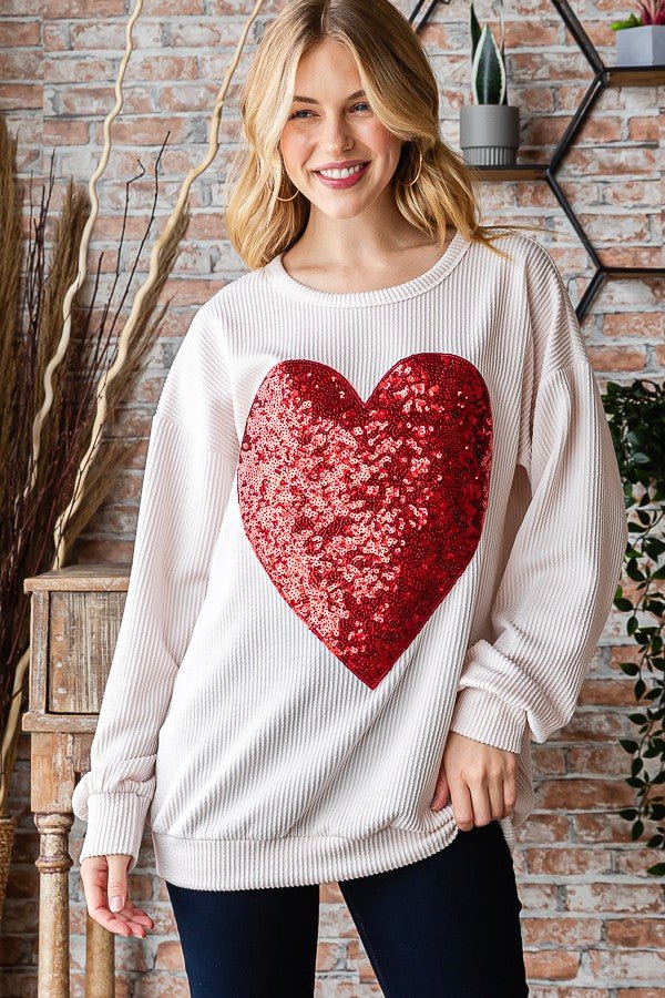 This cream-colored terry cloth ribbed top is perfect for any lovebirds! Long sleeves, a scoop neckline, and a sparkling red sequin heart make it a sweet choice for the upcoming Valentine's Day. Treat yourself or your honeymooner to this darling top!  95% Polyester 5% Spandex