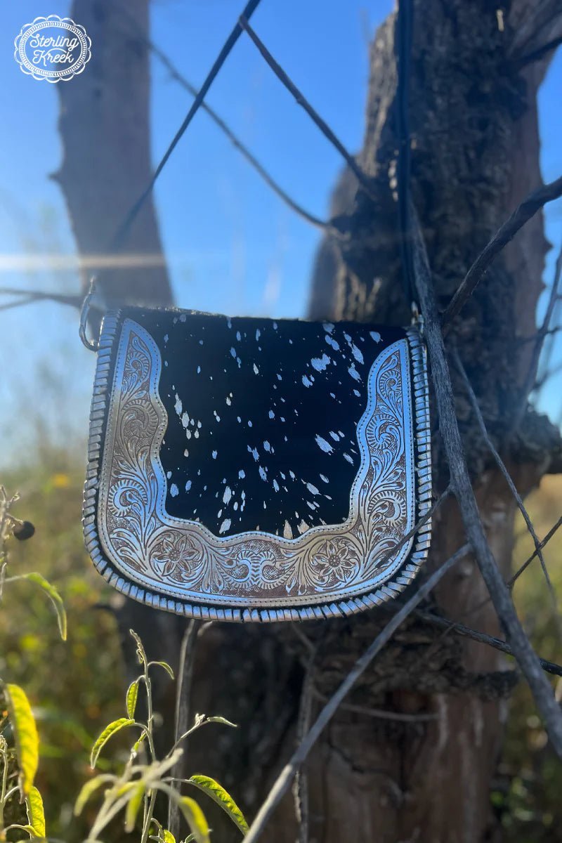 This unique Buckle Babe Bag is a perfect way to show off your style! Crafted with black leather and black cowhide with silver specks, it features a flashy silver tooled belt buckle look for an edgy, eye-catching finish. Ready to turn heads? Wear this bad boy and you'll be sure to do just that!  Button Snap Closure, small zipper on the inside  Adjustable/Removable strap : 58"  width: 9"  length: 8.5"