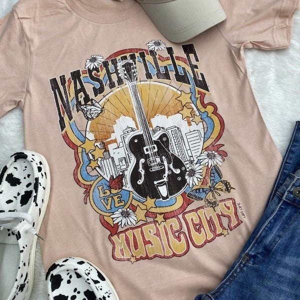 Rodeo up to Music City in this light pink tee - it's your ticket to those colors of Nashville! Featuring a guitar on the Nashville skyline to signify your love of country music, concerts, and wild west fashion, you'll be ready for any show!   