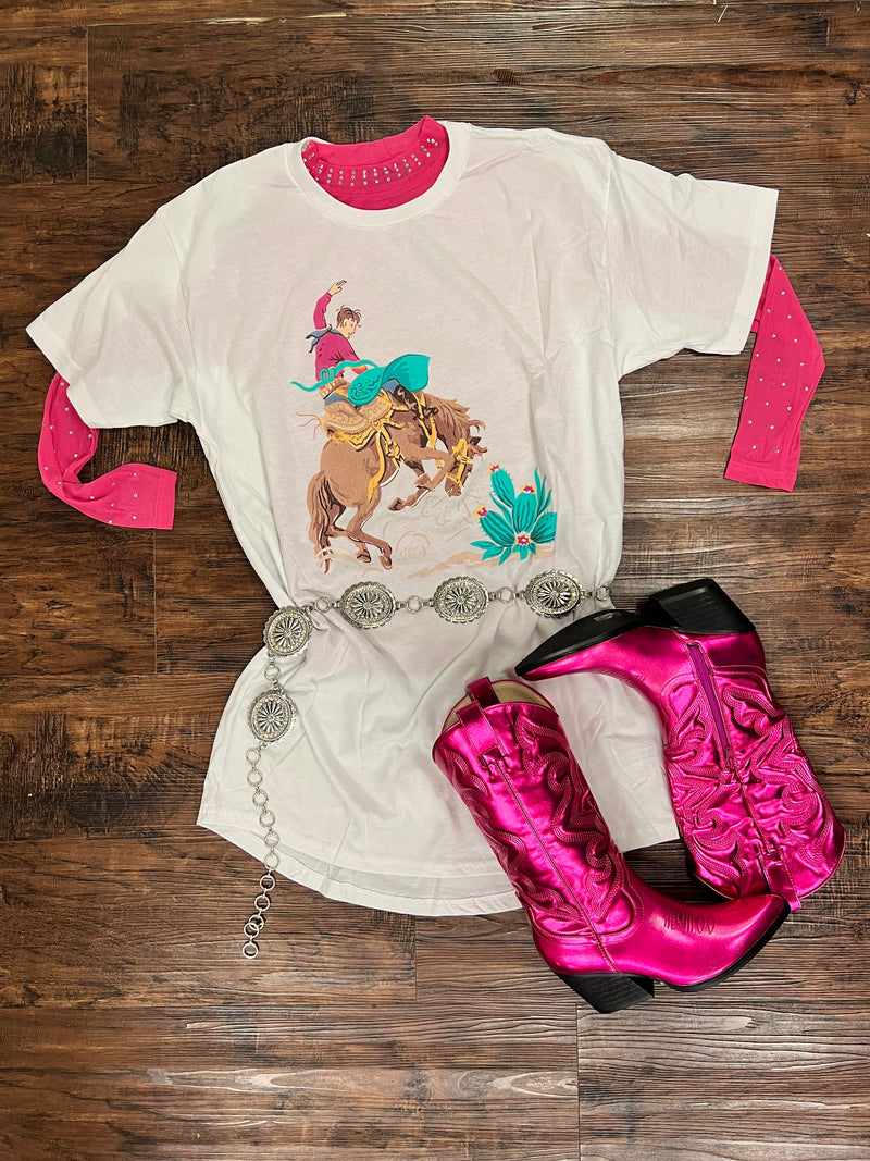 This Bronc Wild TShirt Dress is a can't-miss for wild west-style fans! Featuring a comfy white t-shirt dress with a fun cowboy and bronc on the front and a cactus, this dress is perfect for any rodeo or ranch-style event. Saddle up and take a ride with this stylish getup!  100% COTTON