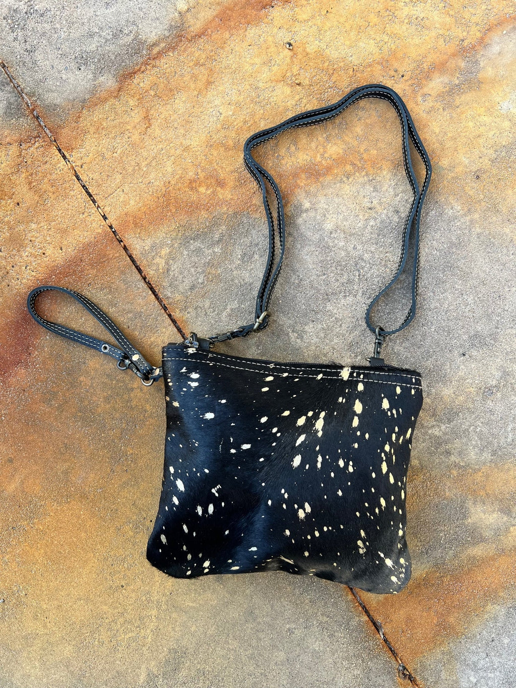 This sleek and stylish Found Gold at Midnight Bag is perfect for making a statement. The luxurious black leather back and soft black hair on hide beautifully contrast the eye-catching gold splatter paint. Its 6" wristlet and 30" shoulder straps make it easy to rock your style any way you please. Live your glamorous life in luxury!