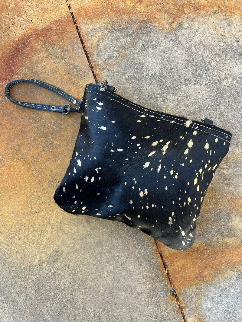 This sleek and stylish Found Gold at Midnight Bag is perfect for making a statement. The luxurious black leather back and soft black hair on hide beautifully contrast the eye-catching gold splatter paint. Its 6" wristlet and 30" shoulder straps make it easy to rock your style any way you please. Live your glamorous life in luxury!