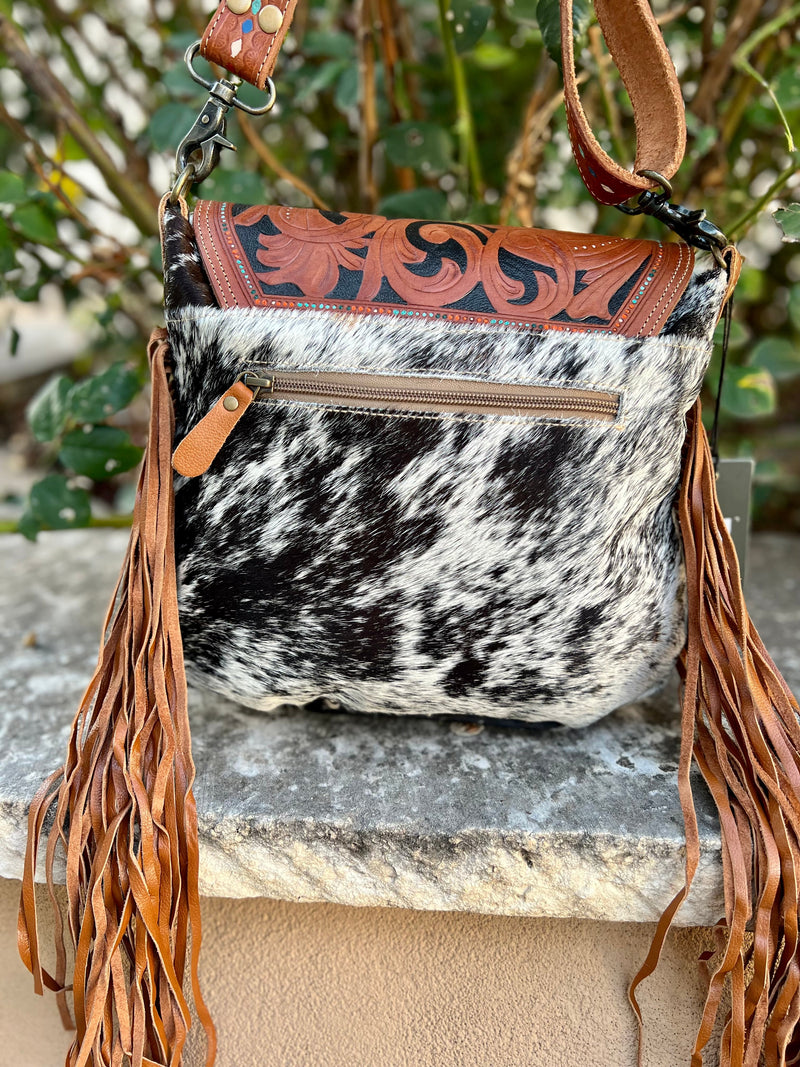 Hair on hide satchel with leather side fringe and tooled leather strap and fold over top closure. Strap is removable and adjustable. Top zip closure under twist latch closure flap. Back is also hair on hide and has a zipper pocket.  12.5"Wx10.5"Hx3"D