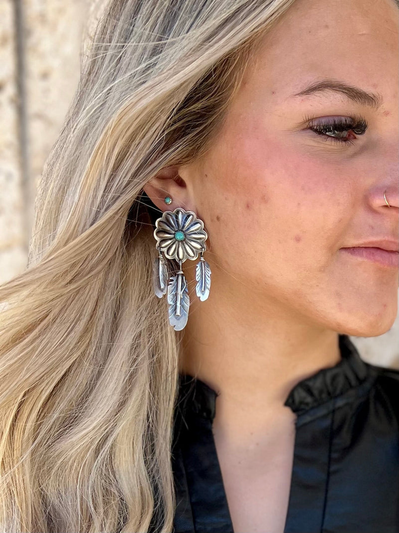 These T'aachill-t'a' Navajo Sterling Silver Earrings add a special touch of class to any ensemble. Handcrafted by Native Americans using genuine Navajo Sterling Silver, they feature a Genuine Turquoise stone and a unique 1" Concho design with 3 Authentic Sterling Silver dangle feathers. Perfect for any occasion.   Measure: 2 1/2" dangle  Suggested Retail:$400.00