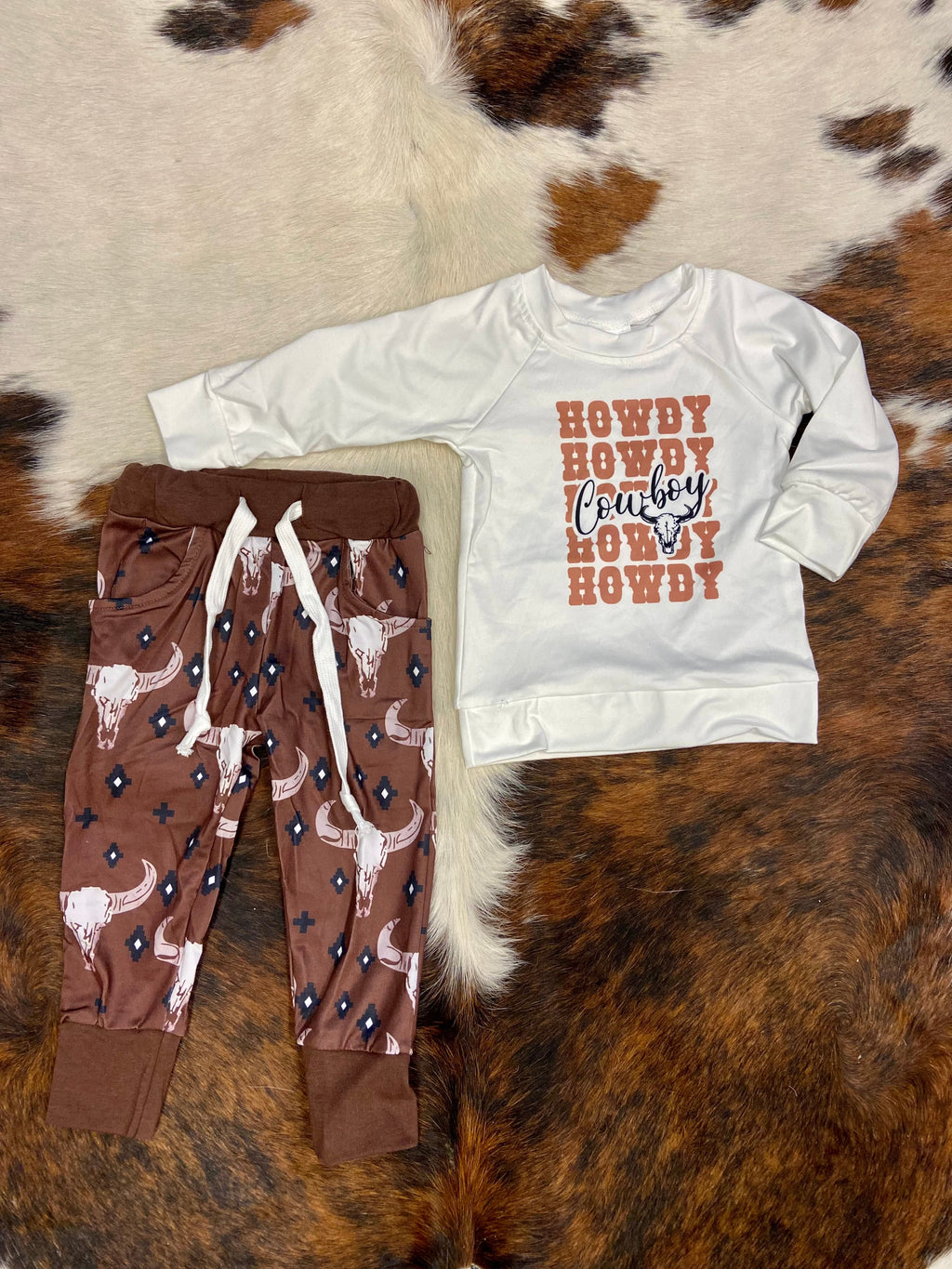 Looking for a rootin’ tootin’ good time? Our Kids Howdy Cowboy Set is just the ticket! This two-piece set is made from butter-soft material, featuring a white long-sleeve top and brown pants with classic cow skulls. Get ready for some wild western fun!