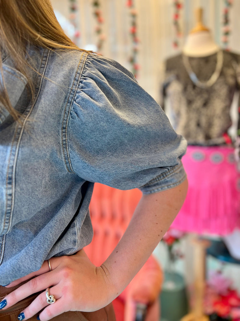 "Get ready to rock the denim trend with The Addyson Top! This short sleeve top features playful puffed sleeves and a stylish bow tie front collar. A must-have addition to any wardrobe for a touch of fun and flair!"