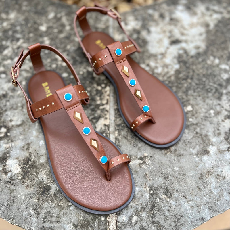 The Turquoise Pocahontas Sandals feature an eye-catching combination of brown flats with turquoise stones and gold grommets for a stylish, comfortable look. Complete your summer wardrobe with this classic strappy sandal.