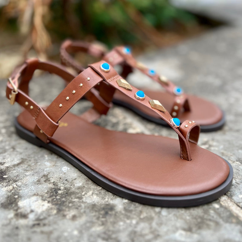 The Turquoise Pocahontas Sandals feature an eye-catching combination of brown flats with turquoise stones and gold grommets for a stylish, comfortable look. Complete your summer wardrobe with this classic strappy sandal.