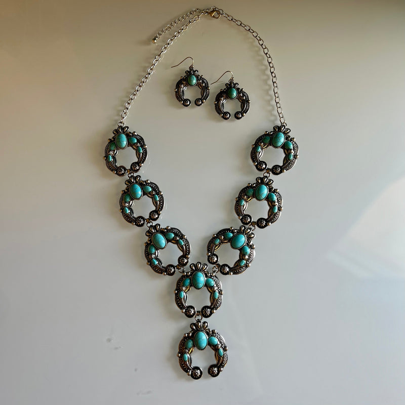 This Up For The Taking Turquoise Squash Set is an exquisite piece. Featuring 8 silver squash blossom conchos inlayed with turquoise stones, the necklace and earrings set is sure to turn heads. Add a touch of classic style and elegance to your look.  28" necklace with 3" adjustable lobster hook clasp