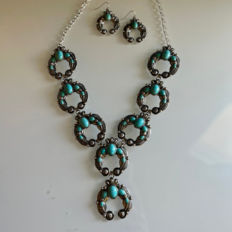 This Up For The Taking Turquoise Squash Set is an exquisite piece. Featuring 8 silver squash blossom conchos inlayed with turquoise stones, the necklace and earrings set is sure to turn heads. Add a touch of classic style and elegance to your look.  28" necklace with 3" adjustable lobster hook clasp