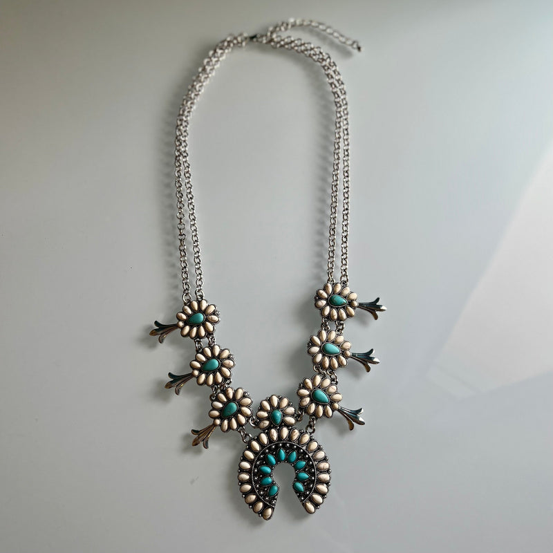 This statement piece is sure to make a statement at any event: the It Takes Two Squash Blossom Necklace. Features include a choice of turquoise or turquoise and white, a 22" silver chain with a 3" adjustable clasp, 7 mini stone conchos for added character, and a double chain with a 2" squash blossom. Feel fashionable and distinctive!