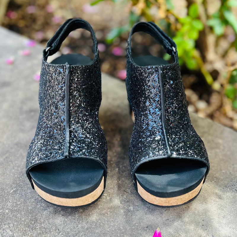 Step out in style with our Black Glittered Comfort Wedges. This eye-catching design features luxurious black glitter and a cork sole for added comfort. The sparkly straps and open toe add a touch of glamour, making these wedges perfect for a night out or special occasion.