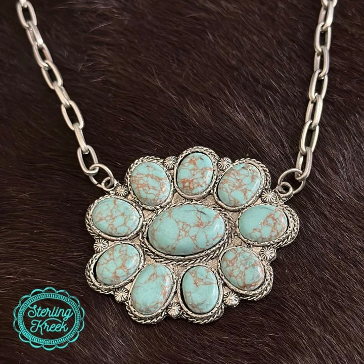 Stand out from the herd with The Jane Necklace! Featuring a Western-inspired turquoise blossom strung on a dainty chain link, this piece will add a touch of sassy-sweet style to any outfit. Get ready to charm 'em, cowgirl!  Length: 11:  extended chain: 3"