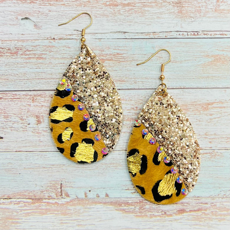 Luxuriate in the wild elegance of these Gilded Leopard Earrings. Crafted from leopard-print hair-on-hide and rose gold glitter, they are finished with gold splatter, iridescent rhinestones, and a 2.5" teardrop shape. Dangling from a fish hook back, these earrings make a lavish addition to your jewelry collection.