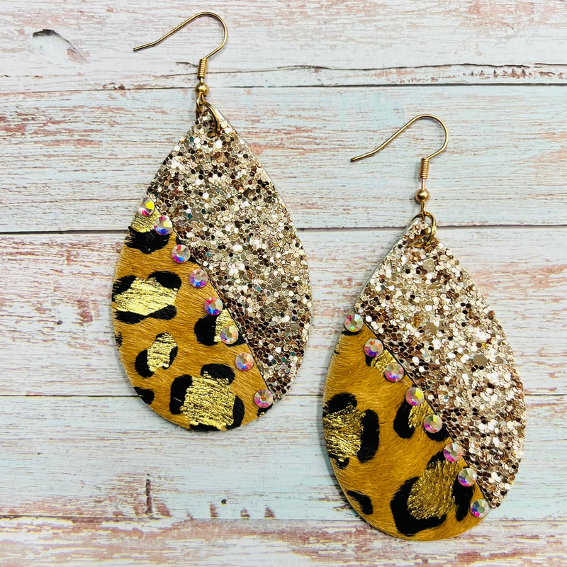 Luxuriate in the wild elegance of these Gilded Leopard Earrings. Crafted from leopard-print hair-on-hide and rose gold glitter, they are finished with gold splatter, iridescent rhinestones, and a 2.5" teardrop shape. Dangling from a fish hook back, these earrings make a lavish addition to your jewelry collection.