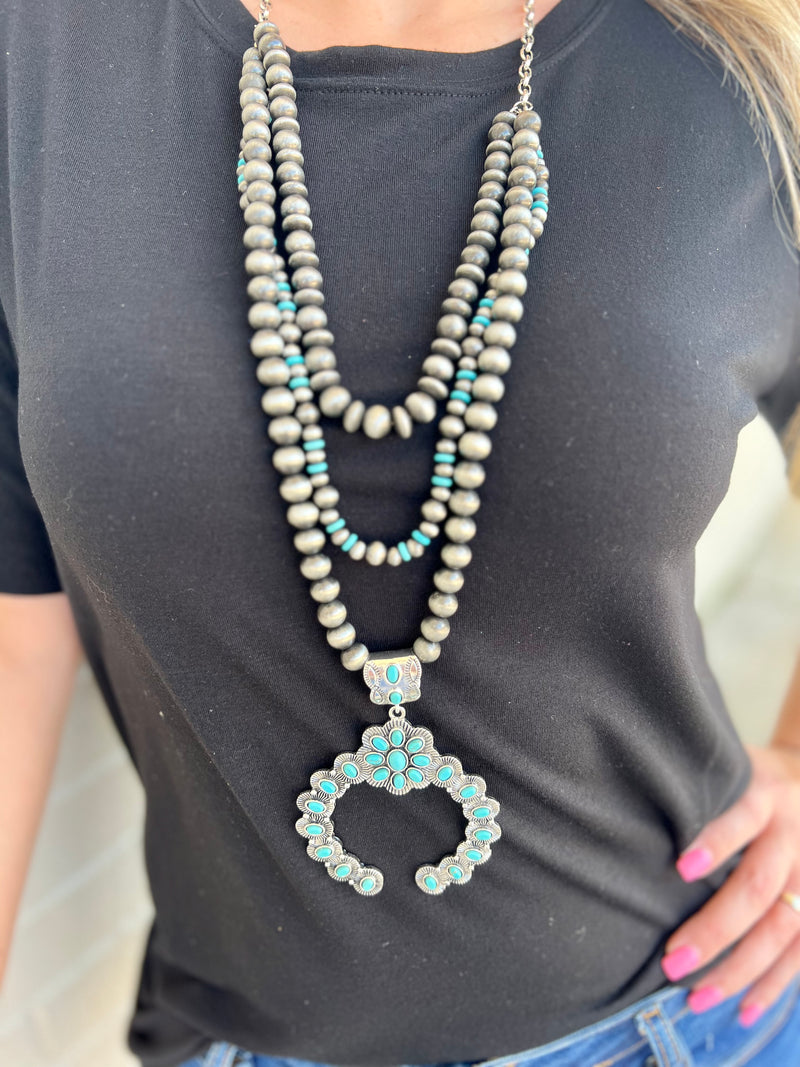 This Never A Third Wheel Necklace is a sophisticated and exclusive western style piece, boasting a triple layered necklace of turquoise stone details, Faux Navajo Pearls, and an intricate squash blossom design. Perfectly crafted to measure 32" in length, this stunning statement piece makes for a timeless addition to any luxury wardrobe.
