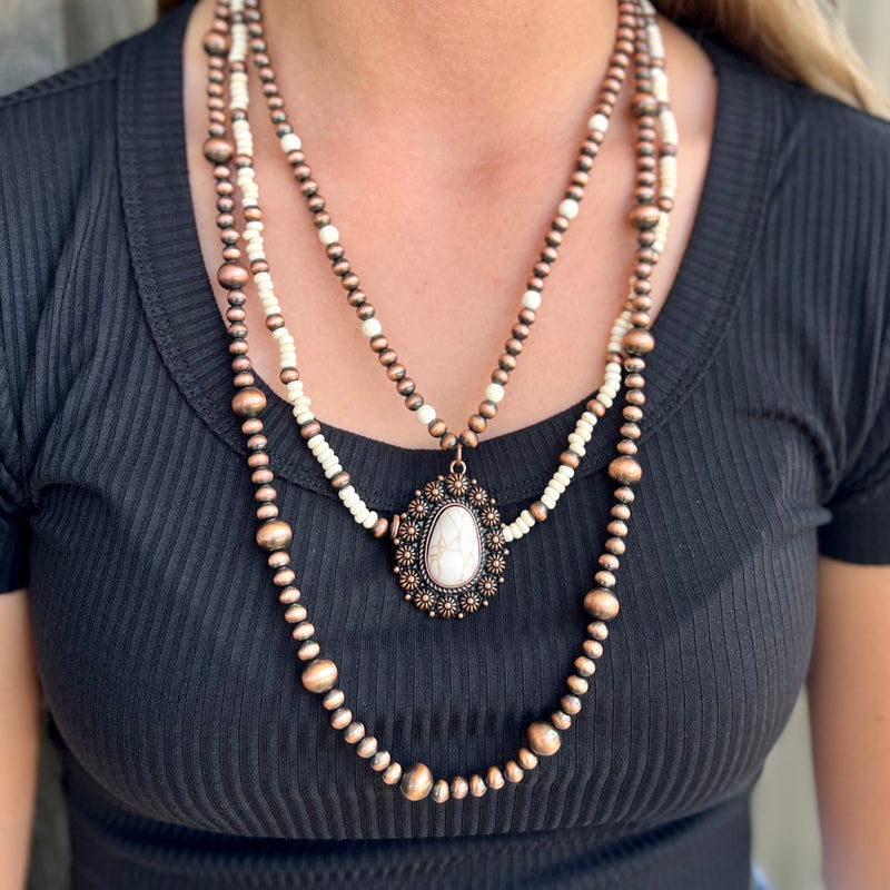 A one-of-a-kind accessory, this Copper Encased Ivory Stone Necklace will add an exclusive touch to your look. This necklace features a layered squash blossom design, with 24" of luxurious copper beads juxtaposed with captivating ivory beads and beautiful stone accents. Perfect for an unforgettable evening out.
