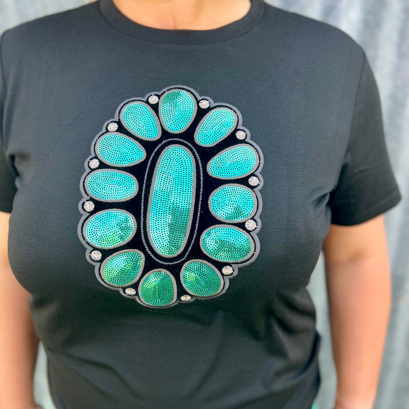 This STREETS OF TURQUOISE TEE will have you looking like a million bucks! Featuring a black tee with a sparkling turquoise sequin concho design in the middle, it's the perfect way to dress up a casual look. Yee-haw!  60% polyester 35% rayon 5% spandex