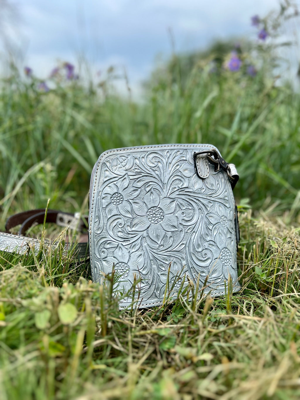 Discover the darling, garden-inspired beauty of this Silver Crossbody. Crafted with an exquisite floral tooled pattern on the front and a large basket weave tooled pattern on the back, this piece adds a subtly sophisticated air to any look. With a generous 9"W X 8"H size and a 50" adjustable and removable strap, this stunning bag offers convenience and effortless style.