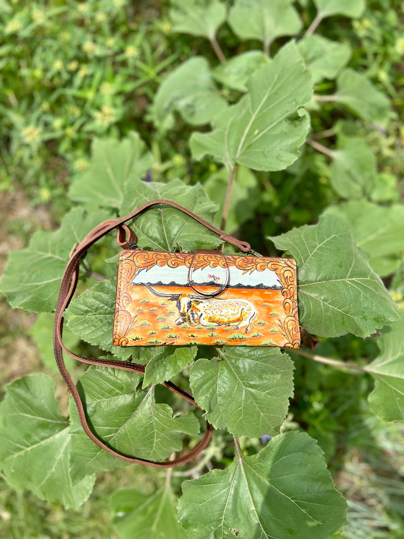 Introducing the Longhorns Horizon Wallet: your stylish, quirky companion on the open plains! This 8"W X 4"H crossbody wallet comes with a 50" adjustable and removeable strap, so you can easily secure it while you're running wild. Plus, it's got a hand painted long horn steer design, fold over snap closure, and multiple card slots and inside zipper compartment to store all your loot! Saddle up!