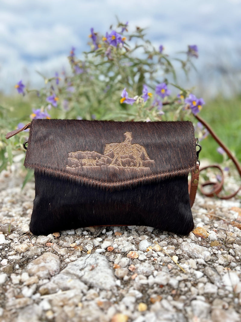 This crossbody is Etched in the Wilderness - crafted from luxurious hair on hide to bring you a bag that makes a statement! From the branded western horseback scene to the zippered compartments, you'll be ready to ride with style and utility. Saddle up and take it out for a spin! 11"W X 8"H  **All Hair On Hides will differ slightly**