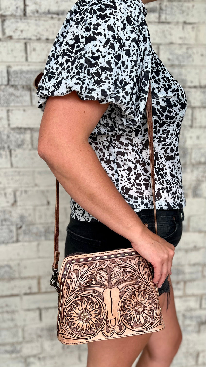 Discover the darling, western inspired beauty of this Longhorn Country Tooled Leather Bag . Crafted with an exquisite floral tooled pattern on the front with a Tooled Longhorn in the center and white buck stitch trim,  this piece adds a subtly sophisticated air to any look. The gorgeous tooled sunflowers make this bag pop. With a generous 9"W X 7"H size and a 50" adjustable and removable strap, this stunning bag offers convenience and effortless style.