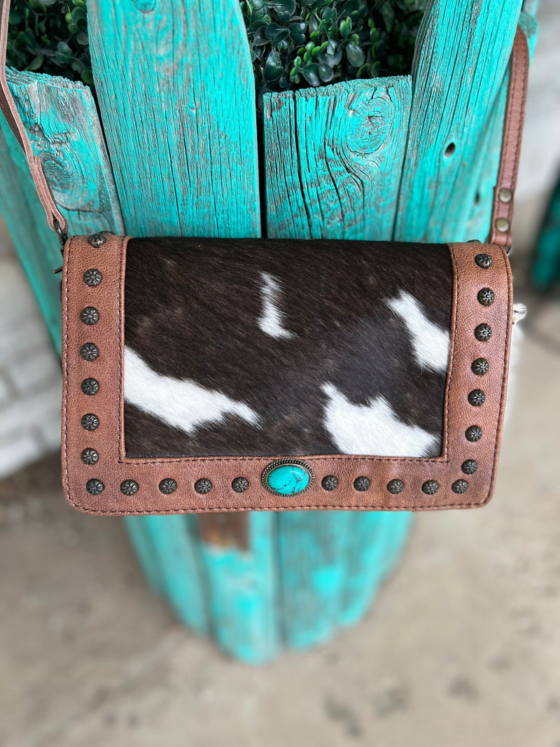 The Studded Darling Crossbody Bag adds a touch of sophistication to any ensemble. Crafted from genuine leather, and available in three different variants of luxurious hair on hide, this eye-catching bag boasts a distinctively studded detail, adding sparkle and texture. Featuring an oval turquoise stone concho, it measures 9"W X 7"H to provide the perfect size for your inspired style.
