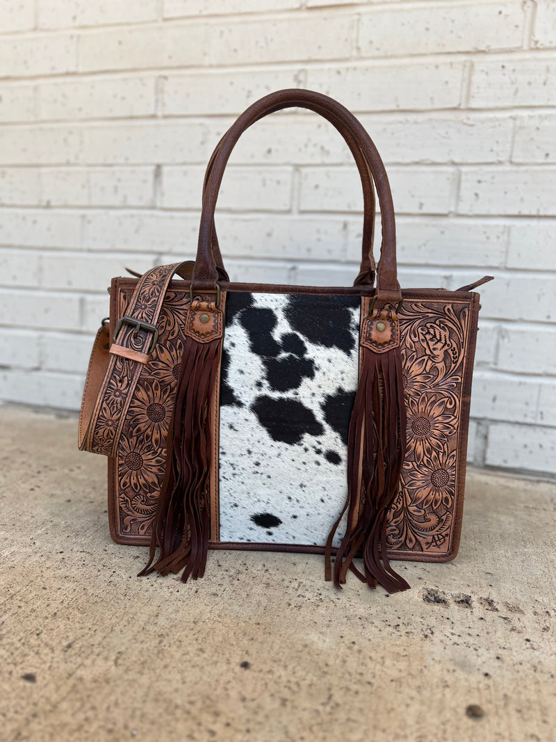 Absolutely beautiful genuine brown spotted hair on hide and brown tooled leather purse! The bag has a large zipper closure pocket, inside zipper pocket, two open pockets. Back is brown leather with concealed carry pocket. Removable tooled crossbody strap. Tassel detail and tooling make it stand out from the crowd!  16"Wx12"Hx5"D  handles: 10"   strap: 22"