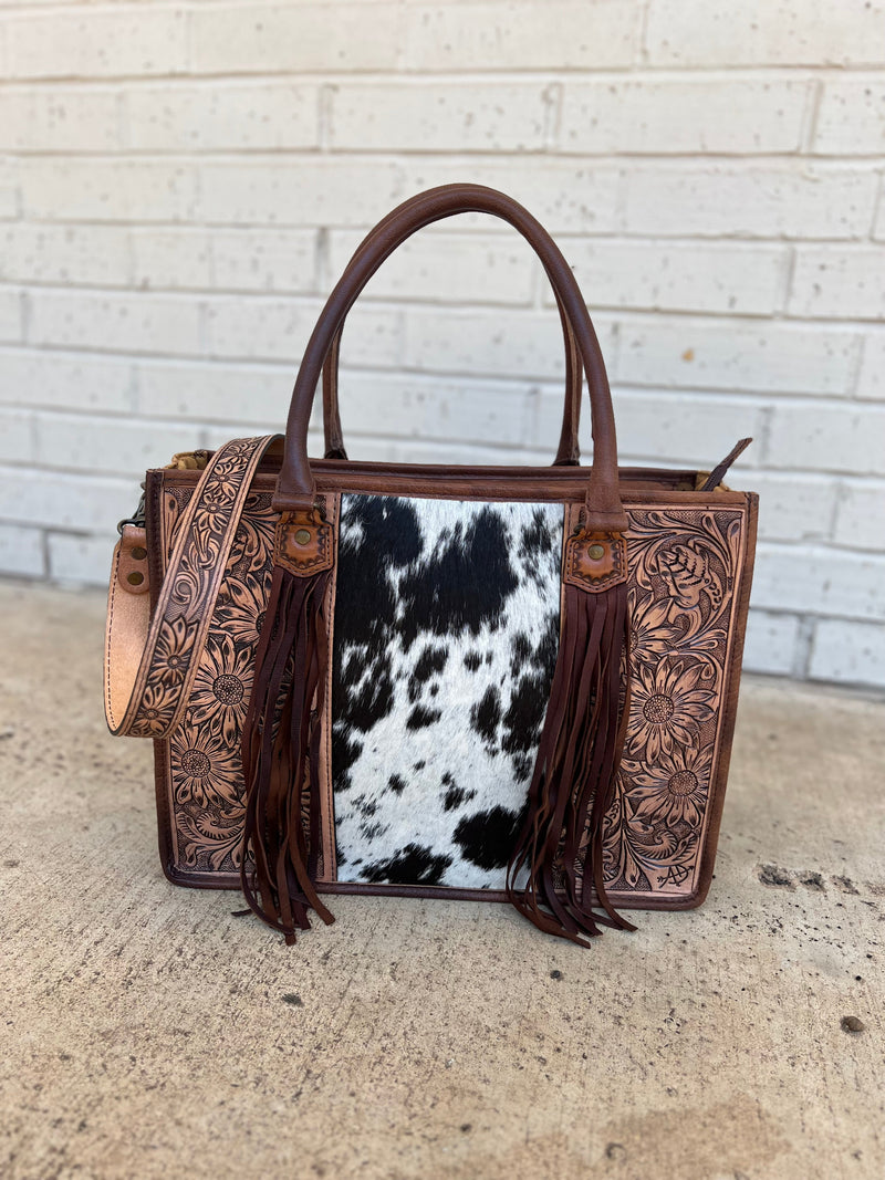 Absolutely beautiful genuine brown spotted hair on hide and brown tooled leather purse! The bag has a large zipper closure pocket, inside zipper pocket, two open pockets. Back is brown leather with concealed carry pocket. Removable tooled crossbody strap. Tassel detail and tooling make it stand out from the crowd!  16"Wx12"Hx5"D  handles: 10"   strap: 22"