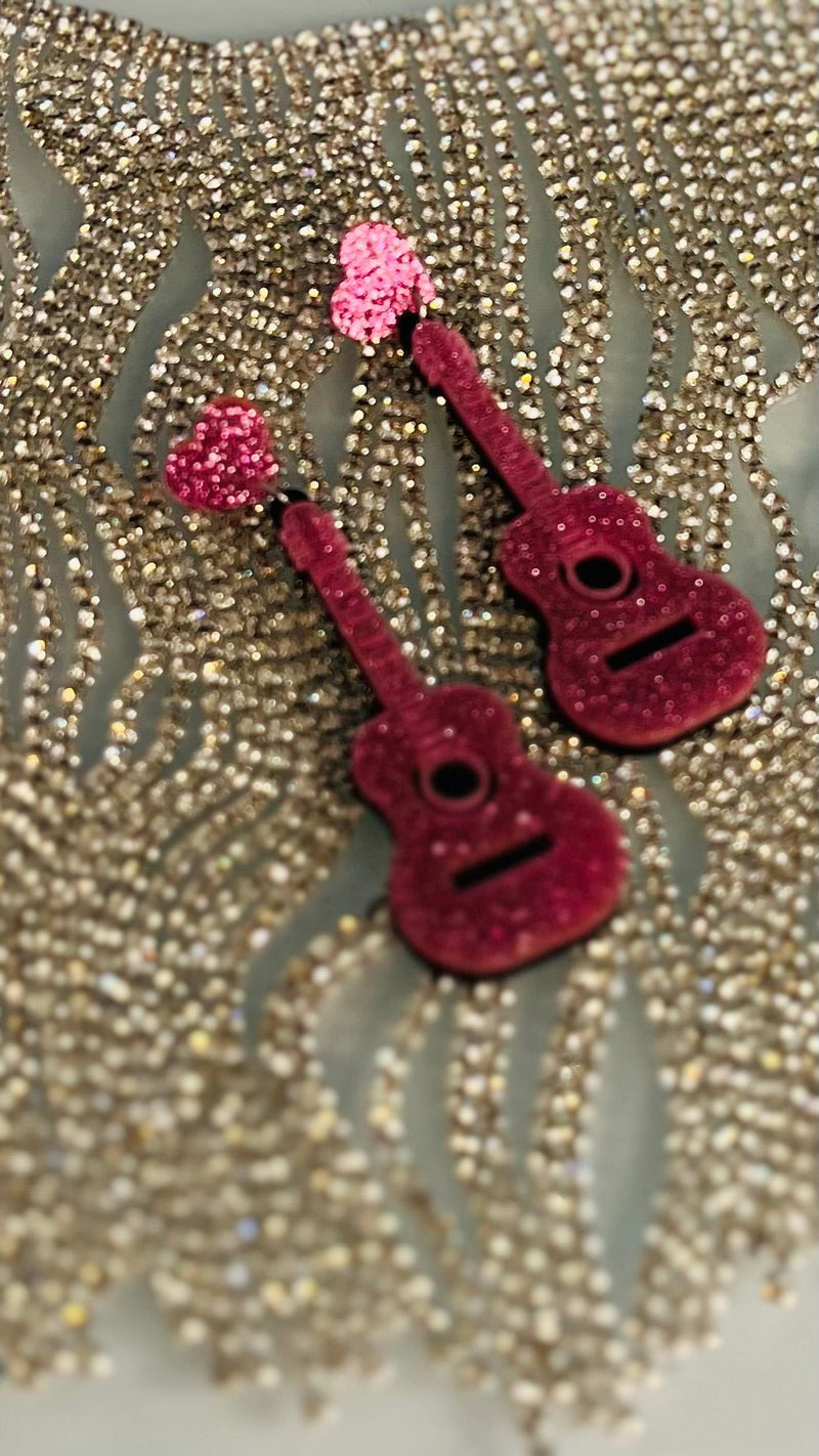 Transform your look with these cool Let's Rock N Roll Girls Earrings! These 3" danglers boast an acoustic guitar in pink glitter with a post back. So rock up your style with these earrings and let the world know you're here to stay! 🎸