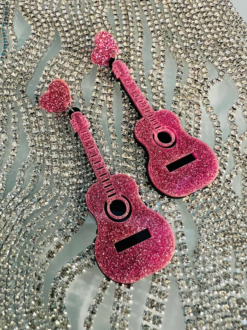 Transform your look with these cool Let's Rock N Roll Girls Earrings! These 3" danglers boast an acoustic guitar in pink glitter with a post back. So rock up your style with these earrings and let the world know you're here to stay! 🎸
