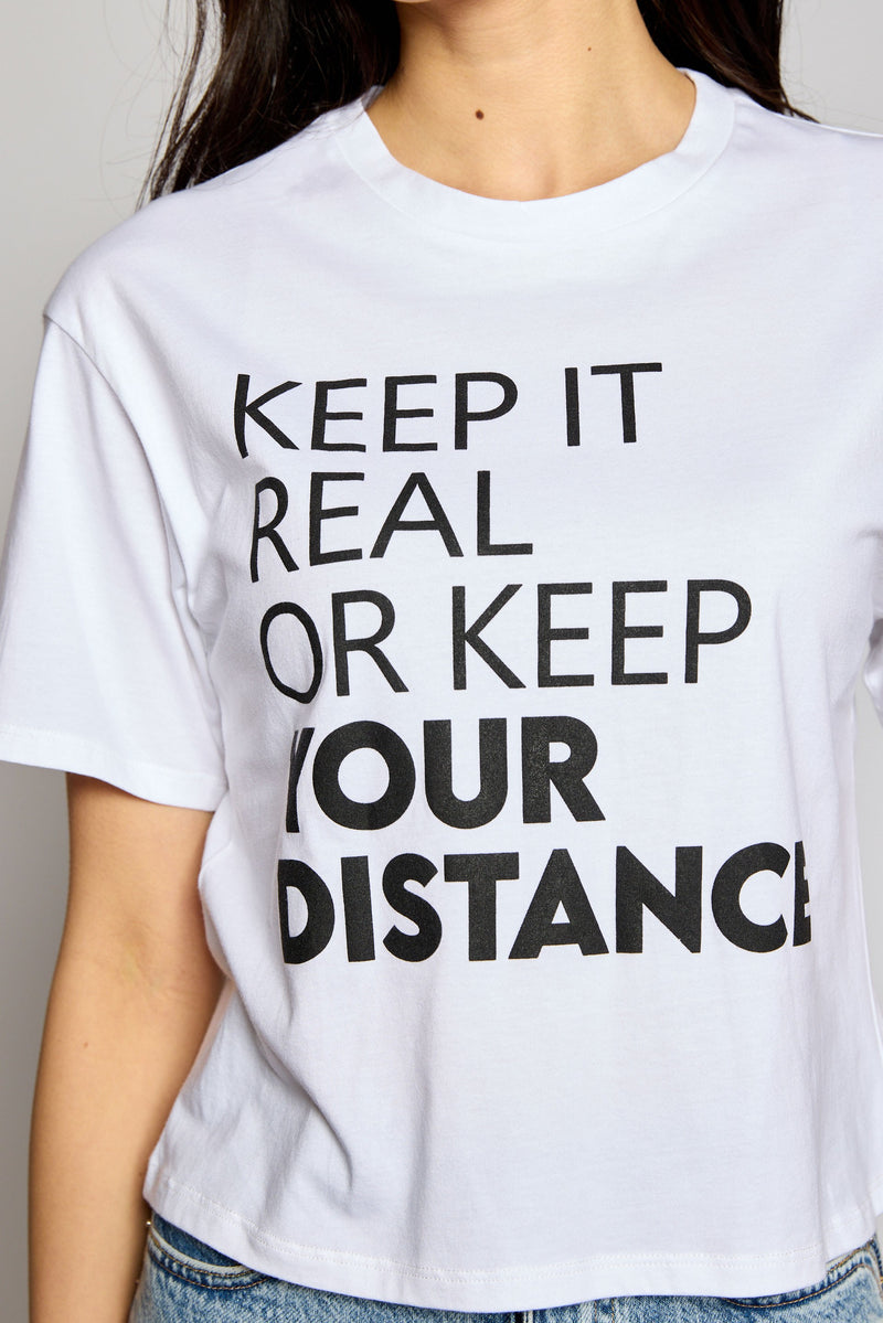 Stay cool and on-trend for the summer in this unique crop top! Be ready for any outdoor activity with this "Keep it real or keep your distance" message. Throw this playful white crew neck top on with your go-to shorts and you'll be ready to tackle the day!