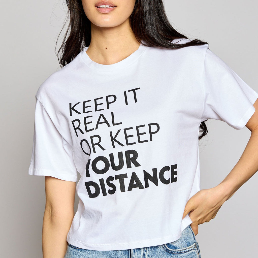 Stay cool and on-trend for the summer in this unique crop top! Be ready for any outdoor activity with this "Keep it real or keep your distance" message. Throw this playful white crew neck top on with your go-to shorts and you'll be ready to tackle the day!