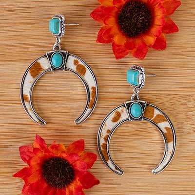 Exuded with classic elegance, these "She's Herding Cattle" Earrings feature a captivating turquoise stone stud and a striking brown and white hair on hide backdrop, encircled by a silver squash blossom design. Handcrafted with creativity and sophistication, these post back earrings are a perfect addition to any luxury wardrobe.