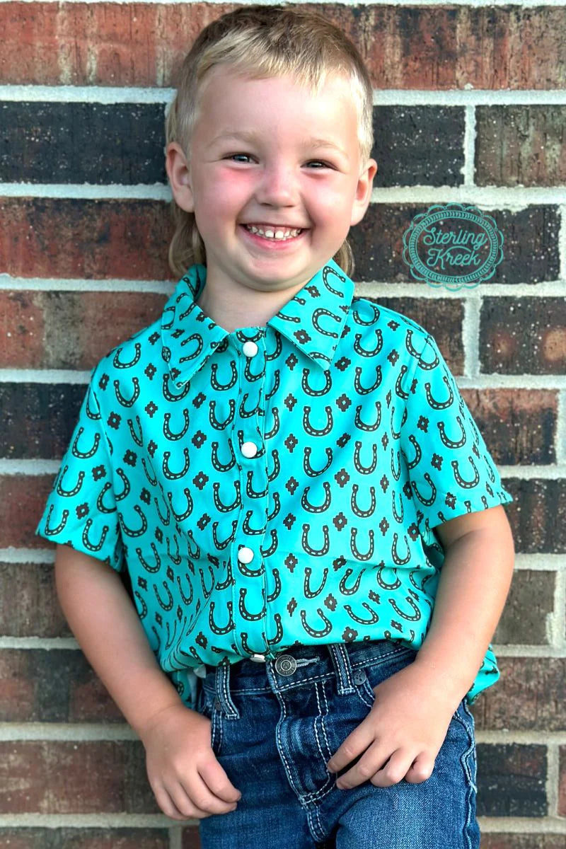 Let your little one look like a true Texas cowpoke with this Lucky Vaquero Top! The turquoise short sleeve design features pearl snaps, and is adorned with a unique brown horseshoes and texas stars pattern. Perfect for wrangler-istas of all sizes!  95% poylester 5 % spandex