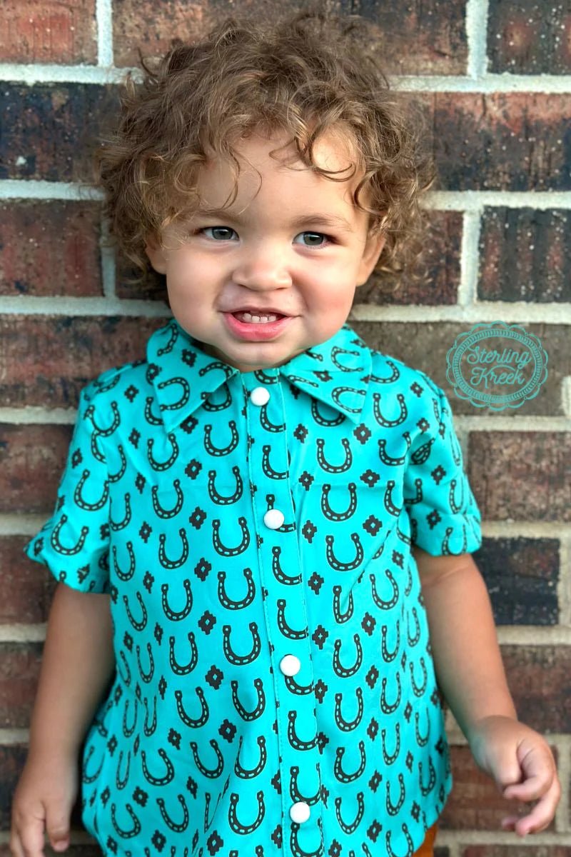Let your little one look like a true Texas cowpoke with this Lucky Vaquero Top! The turquoise short sleeve design features pearl snaps, and is adorned with a unique brown horseshoes and texas stars pattern. Perfect for wrangler-istas of all sizes!  95% poylester 5 % spandex