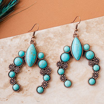 These Western Luck Earrings feature a classic and timeless design with copper and turquoise stones, expertly crafted into a delicate small squash blossom shape. Perfect for any occasion, these earrings are sure to add a touch of Western charm and stylishness. The fish hook backings ensure that you will remain comfortable throughout the day. 2" in length.