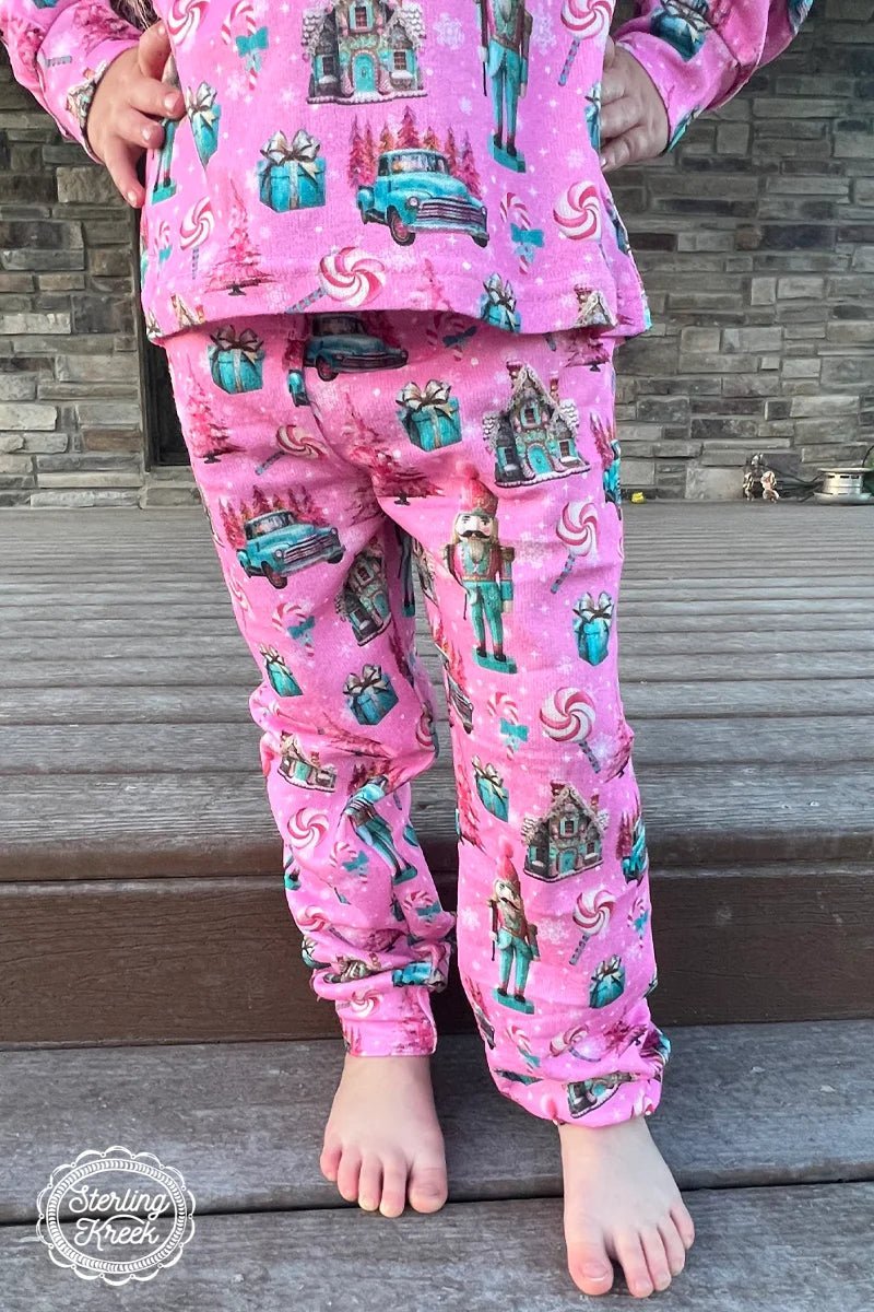 These adorable Mini Son Of A Nutcracker Jam Pants are sure to bring festive cheer to even the grumpiest Scrooge. The pink pants feature turquoise presents, an old vintage truck, pink peppermint lollipops, and a turquoise and pink nutcracker – what more could you ask for? Spread the holiday spirit wherever you go!