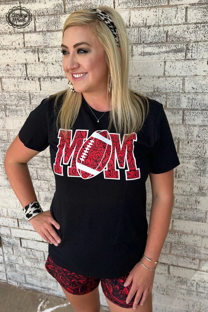 Show your support for your favorite football player, and look good doing it with this stylish Football Mom Tee! The black shirt features a unique tooled print of the word 'MOM' with a football cleverly used to make up the 'O'. Perfect for tailgates and Sunday Fundays alike!