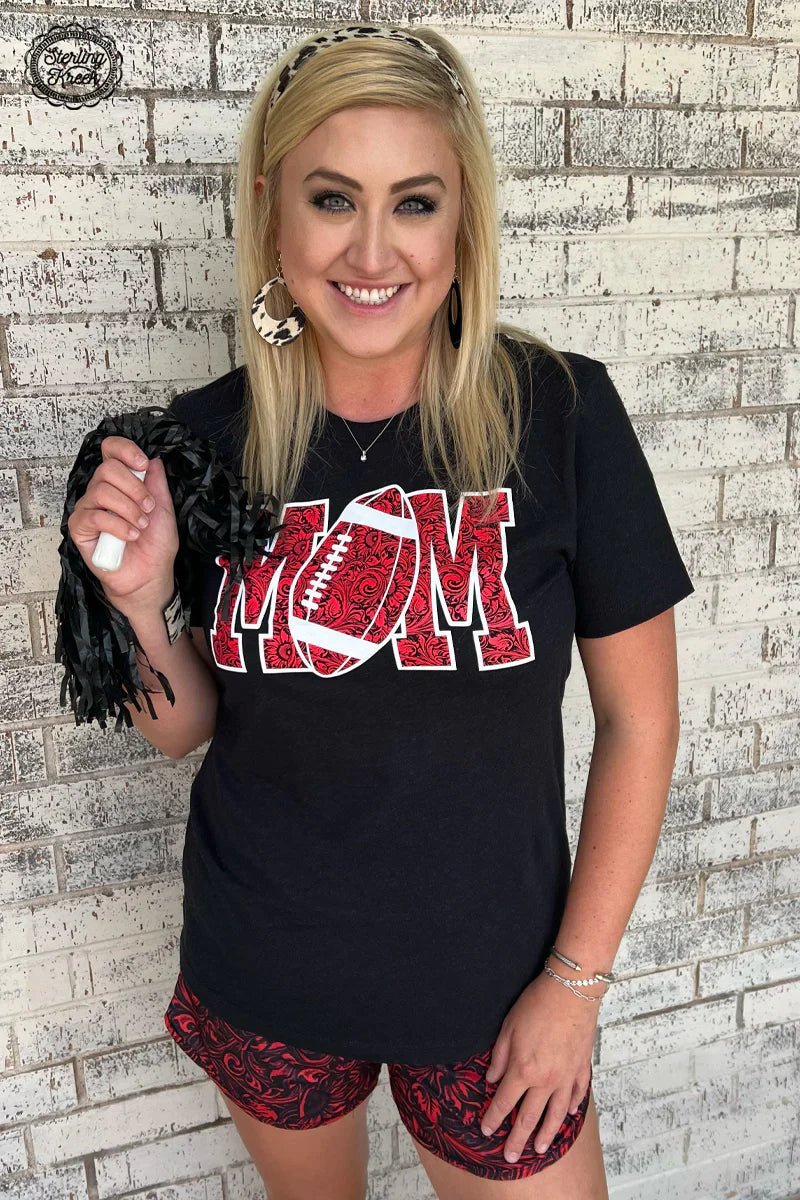 Show your support for your favorite football player, and look good doing it with this stylish Football Mom Tee! The black shirt features a unique tooled print of the word 'MOM' with a football cleverly used to make up the 'O'. Perfect for tailgates and Sunday Fundays alike!