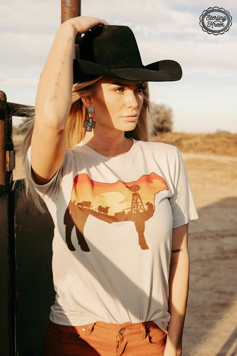 This tan tee has a picture-perfect design of a steer silhouetted in orange hues from a gorgeous sunset. The unique design shows cows milling around a windmill on the inside of the steer. Cowabunga!