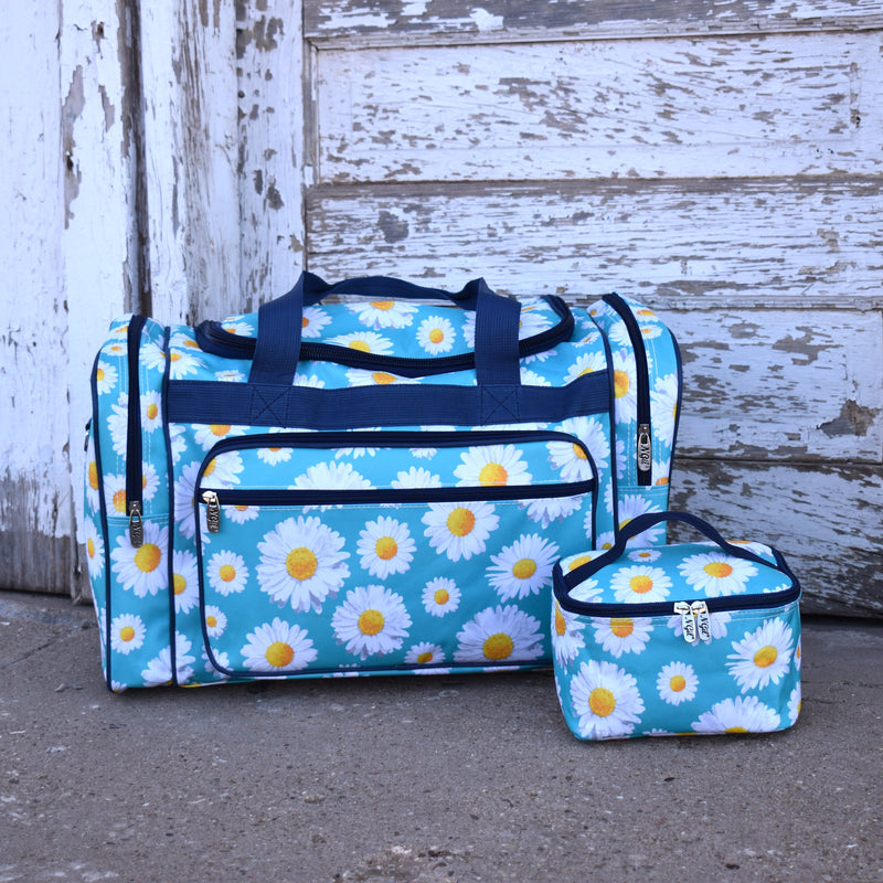Large sky blue vinyl duffle travel bag with all over white daisy print and navy handles, next to matching cosmetic case.