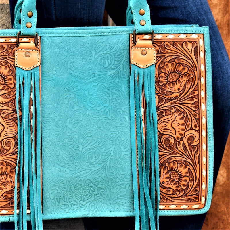 Absolutely beautiful turquoise embossed suede and tan tooled leather purse! The bag has a large zipper closure pocket, inside zipper pocket, two open pockets, and back that is capable for carrying concealed. Comes with a removable tooled leather strap. Front tooled panels have an ivory lacing detail and suede tassel by the handles.