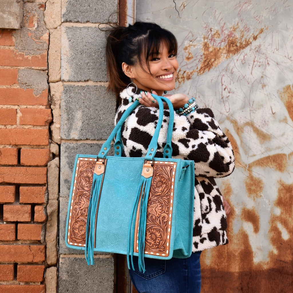 Absolutely beautiful turquoise embossed suede and tan tooled leather purse! The bag has a large zipper closure pocket, inside zipper pocket, two open pockets, and back that is capable for carrying concealed. Comes with a removable tooled leather strap. Front tooled panels have an ivory lacing detail and suede tassel by the handles.