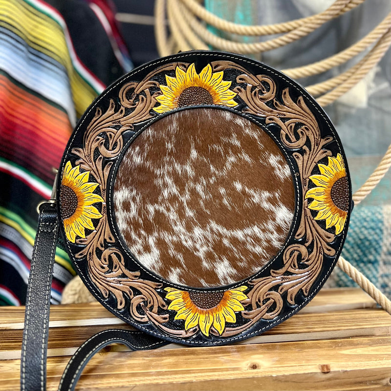 The Canteen In a Blooming Field Bag is a 10" round Hair On Hide with Beautiful Sunflower Tooled Black Leather Accents. The bag features a 3/4 zipper closure and a small zipper closure on the back. The bag features 2 different cowhide variants.    10" round in size and 2" Wide.   48" adjustable strap 