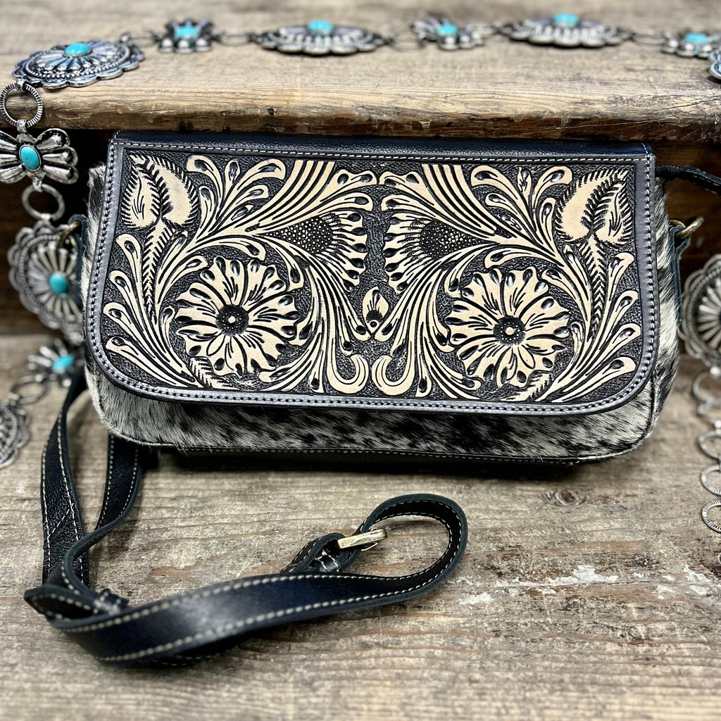The Trillion Hand Tooled Bag is a Black and White Hair On Hide Bag with a Floral Tooled Leather Fold Over Flap. The leather is black as well. The bag is very cute and just the right size.   Dimensions: 11" L X 6" H  Strap: 42" Adjustable/Removable