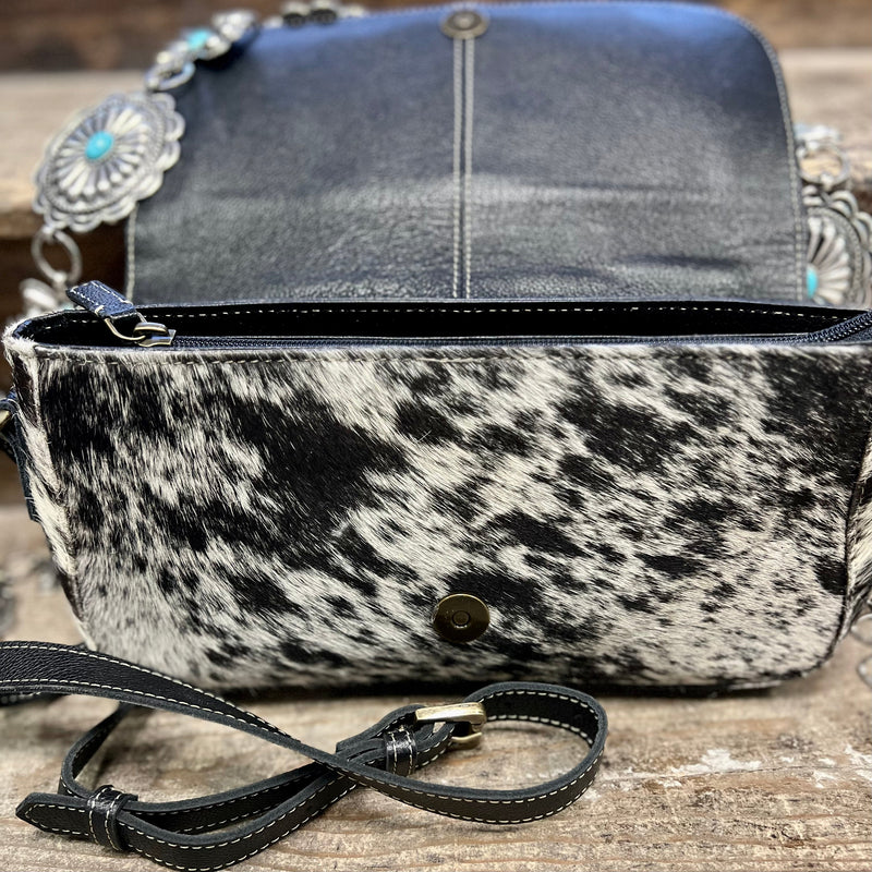 The Trillion Hand Tooled Bag is a Black and White Hair On Hide Bag with a Floral Tooled Leather Fold Over Flap. The leather is black as well. The bag is very cute and just the right size.   Dimensions: 11" L X 6" H  Strap: 42" Adjustable/Removable