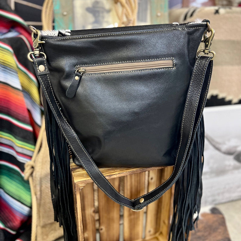 Made By Myra Handbags  The Ajo Leather Bag is a Hair on Hide Bag with a  Hand Tooled Leather fold over flap. The Bag is Cowhide covered and offers 3 different variants.  There is black leather fringe on each side to add lots of character. This bag has a top zipper closure and a zipper compartment of the back side. The strap is a 30 " and is adjustable/removable.  Dimensions: L  12" X H 12"  Strap: Adjustable up to 30"